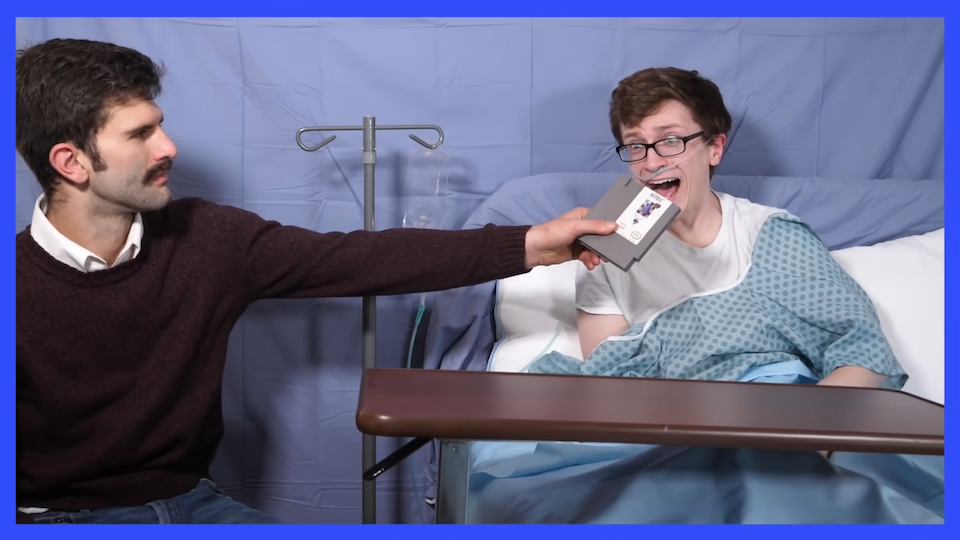 Scott, a brown-haired white guy with glasses, sits in a hospital bed. His therapist Jerry, a white guy with a big mustache wearing a maroon sweater, holds up a copy of Tetris on the NES. Scott screams. There is a thick blue border around the whole image.