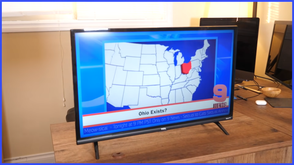 A TV screen showing a news broadcast; there is a graphic of the United States, with Ohio highlighted in red. Its caption reads 'Ohio Exists?'. There is a thin blue border around the whole image.