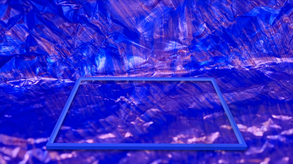 A blue rectangle lies in a blue, iridescent, plastic-wrap-like room. There is no border around this image.